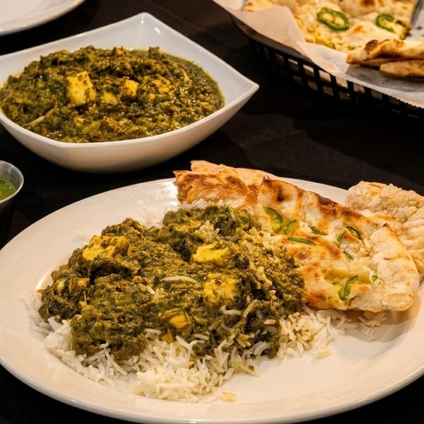 Indian meal with palak paneer, rice, naan bread, and green chutney on a dark table.