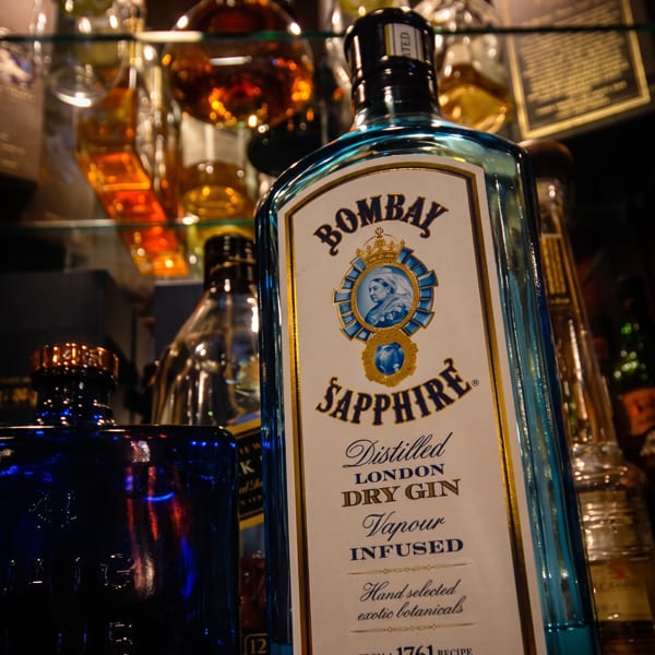 Bombay Sapphire gin bottle prominently displayed on a bar shelf with other liquor bottles.