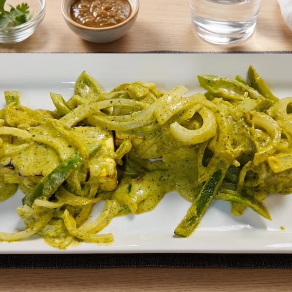 Green curry chicken with sliced onions and peppers on a white rectangular plate.