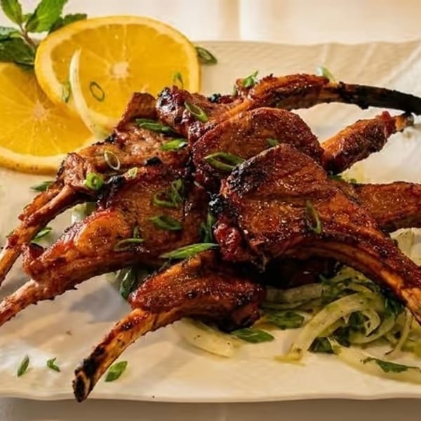 Grilled lamb chops with sliced oranges, mint, and green onions on a white plate.