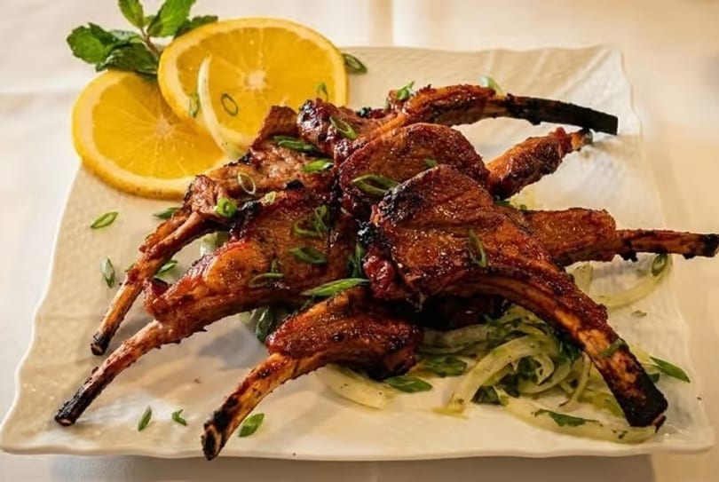 Grilled lamb chops with sliced oranges, mint, and green onions on a white plate.