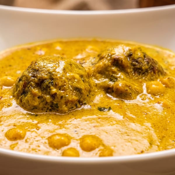 Two large meatballs in a rich yellow curry sauce, served in a white square bowl.