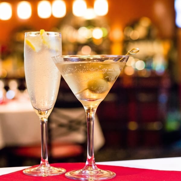 Two cocktails, a martini and a sparkling drink, on a red and white table in a restaurant.
